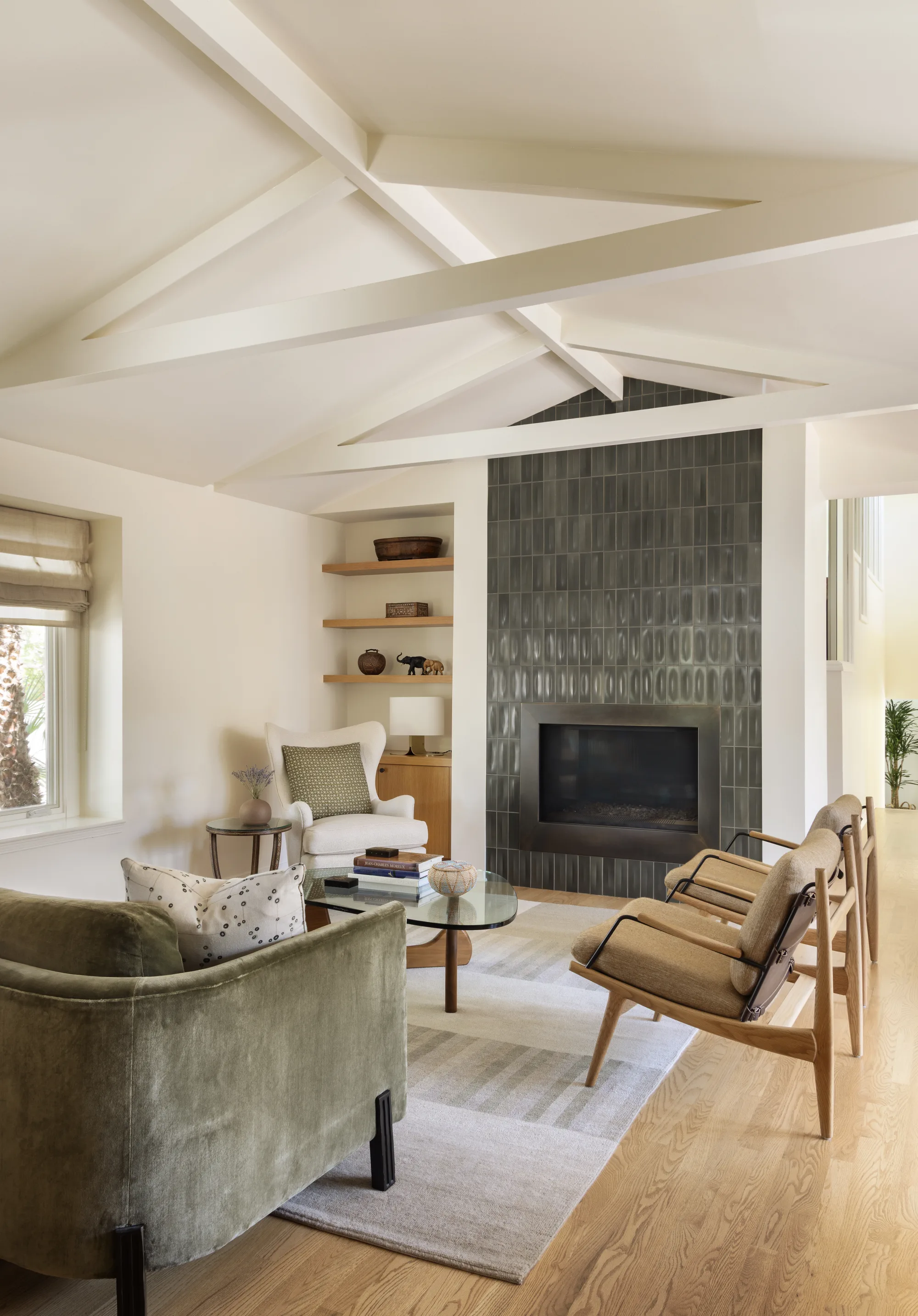 Living room under a white beamed ceiling, with a green velvet chair and a tiled fireplace