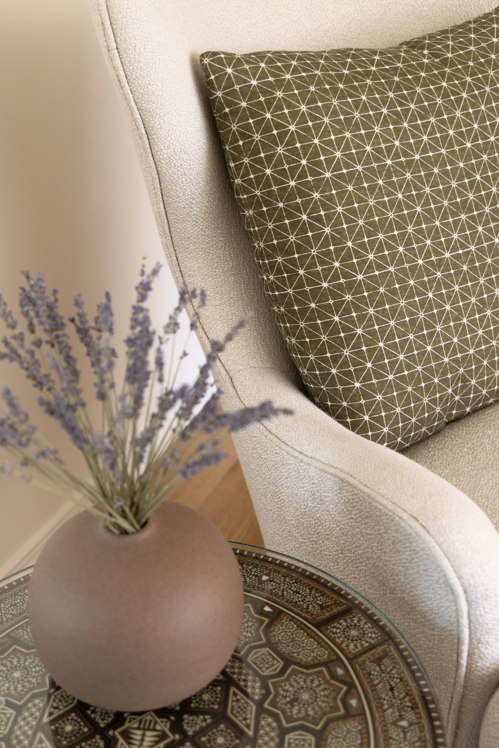 Lavender in a round vase beside a white armchair and a patterned pillow