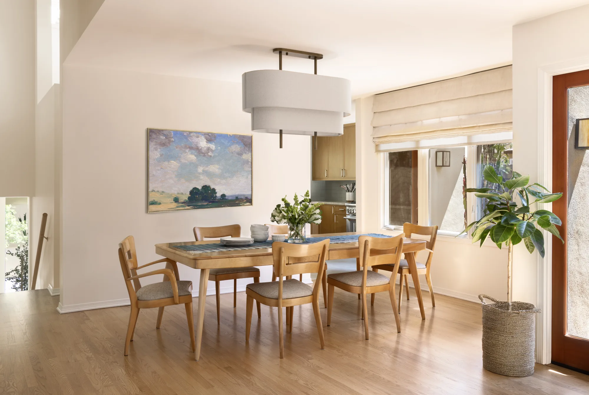 Dining room with a long wood table, a drum pendant and a California landscape painting