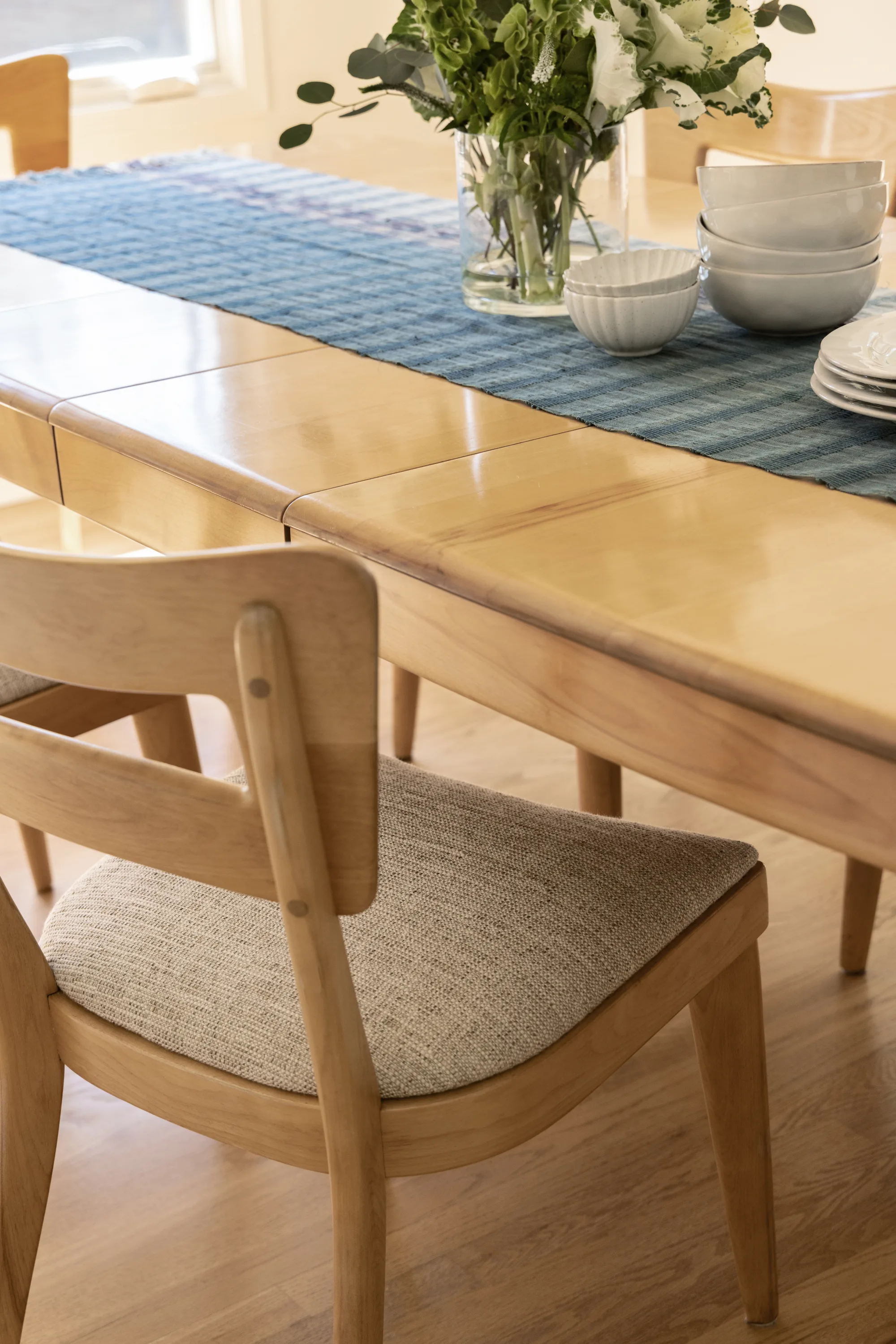 Detail of a wood dining chair and table set with a blue runner and white dishes