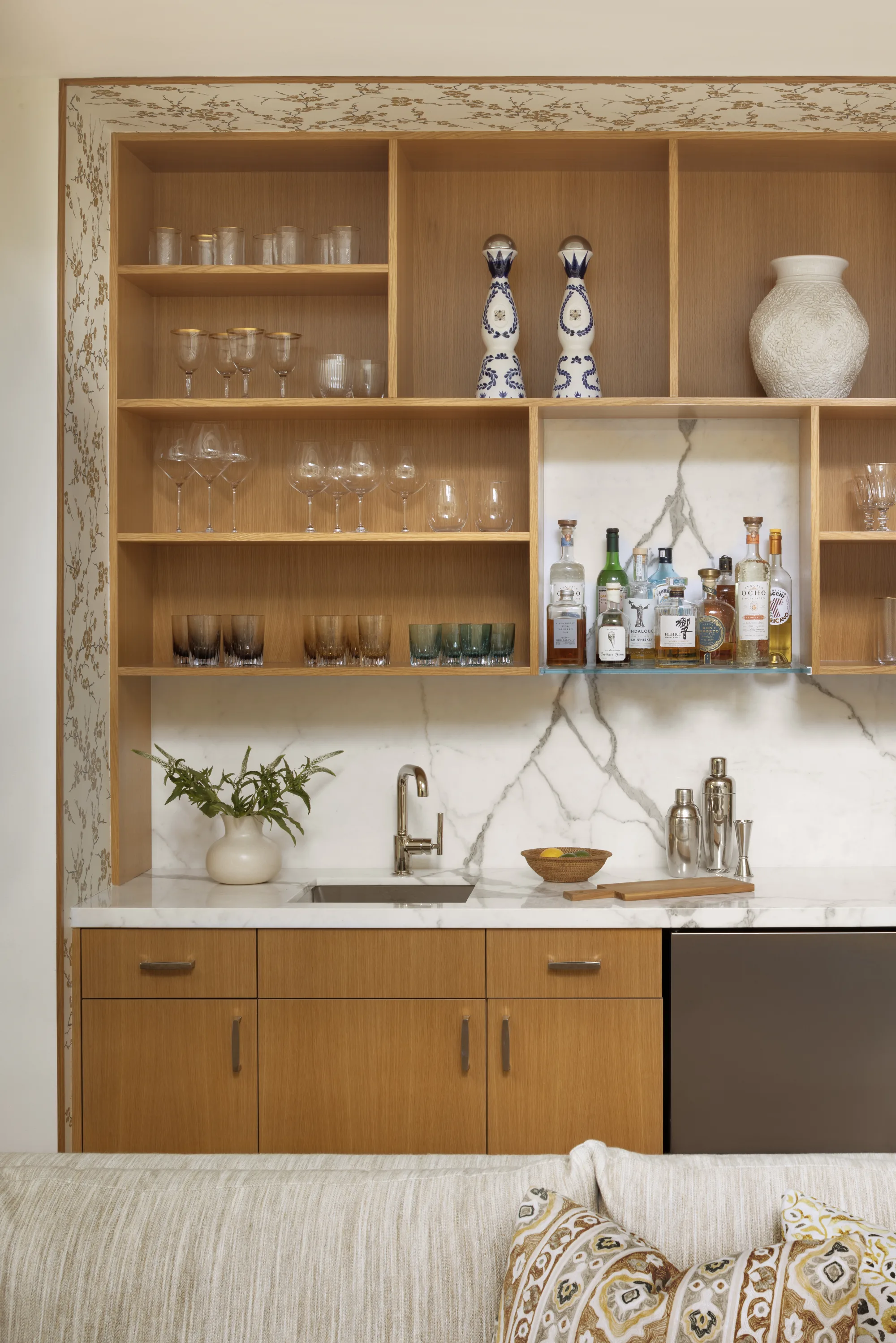 Wet bar with open oak shelving, glassware and a marble backsplash