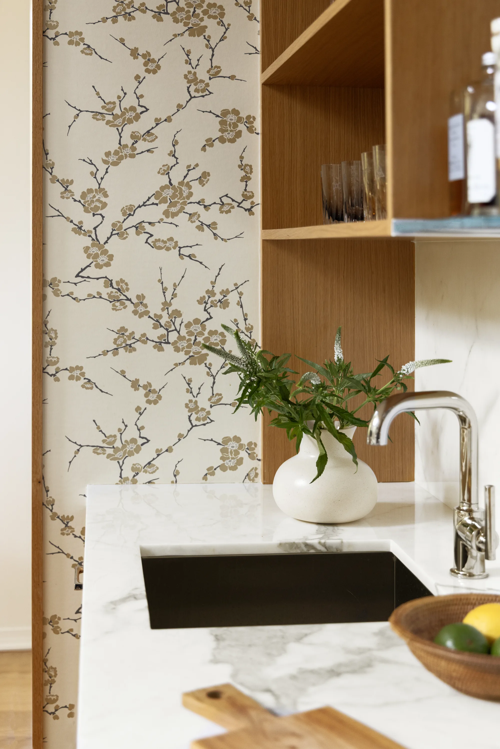 Bar sink with a marble counter beside blossom-print wallpaper