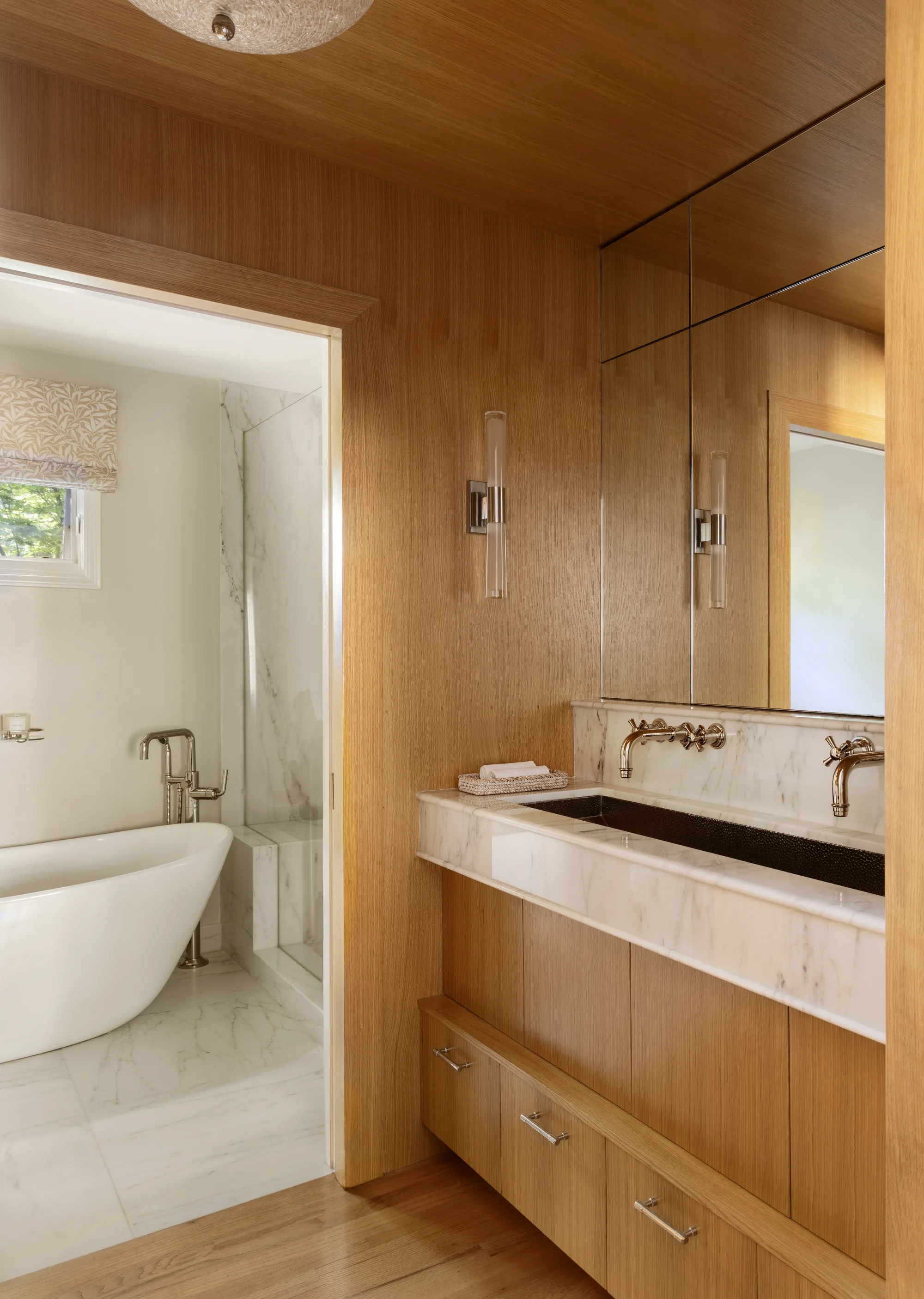 Oak-paneled bathroom with a stone trough sink opening onto a freestanding tub