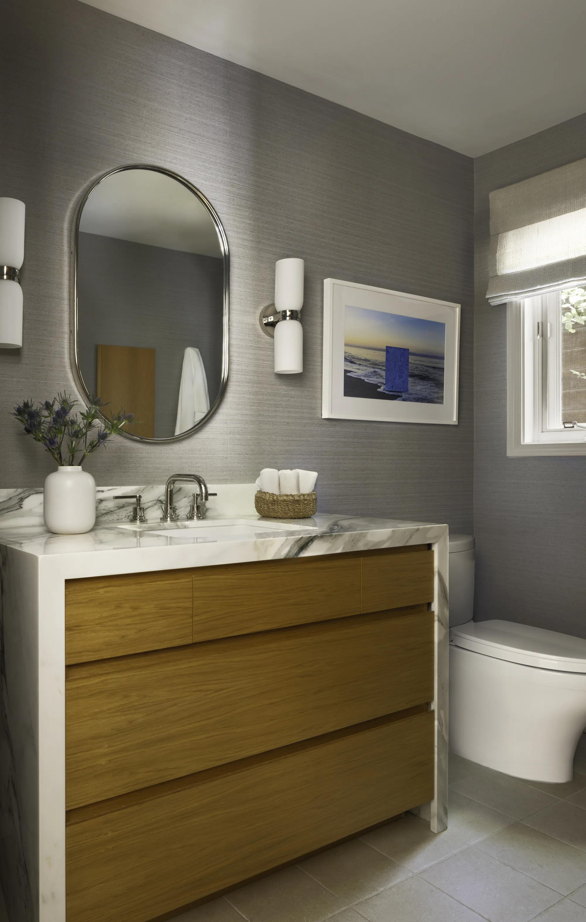 Powder room with an oak vanity, a marble top and an oval mirror