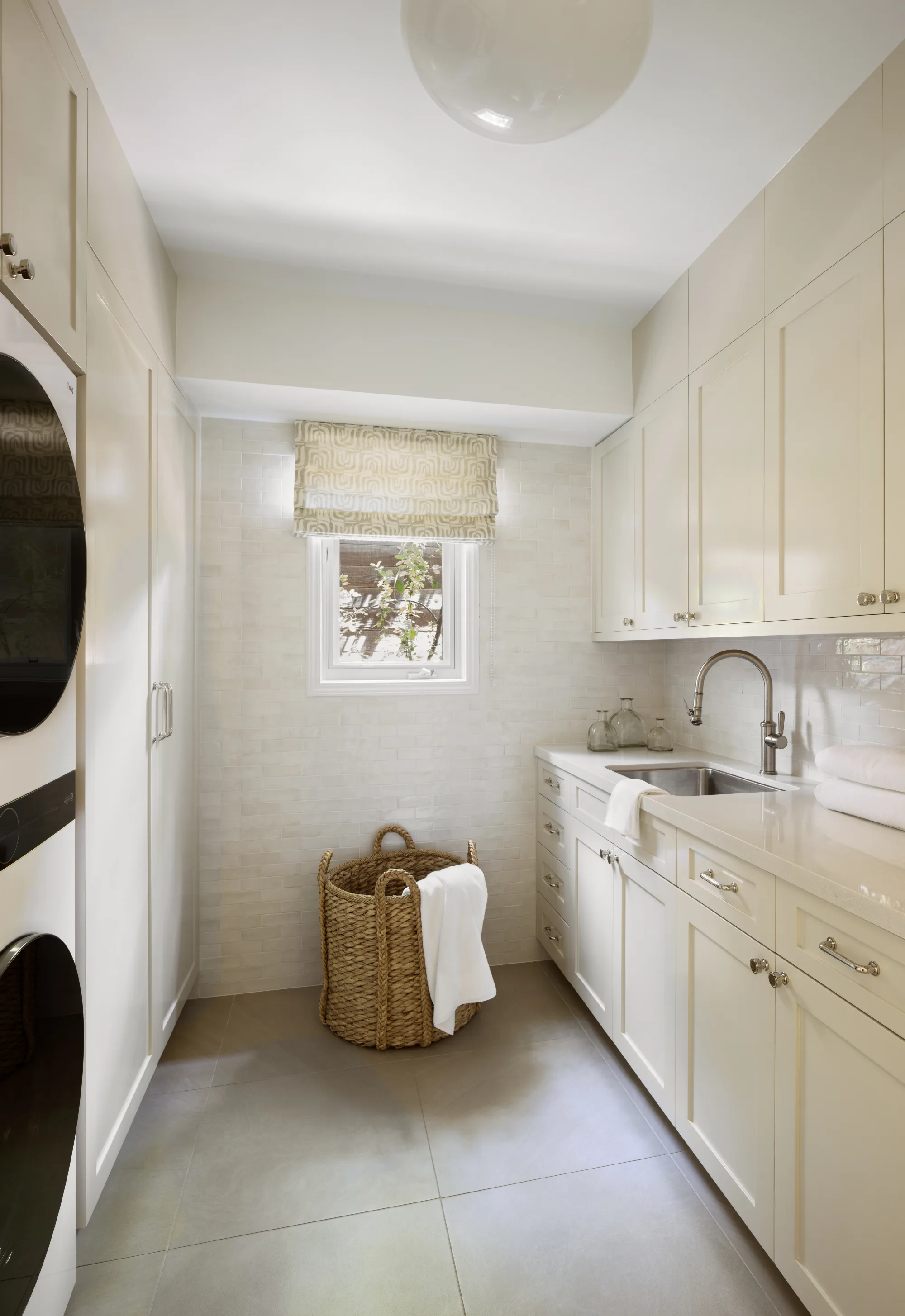 Laundry room with white cabinetry, stacked machines and a woven basket