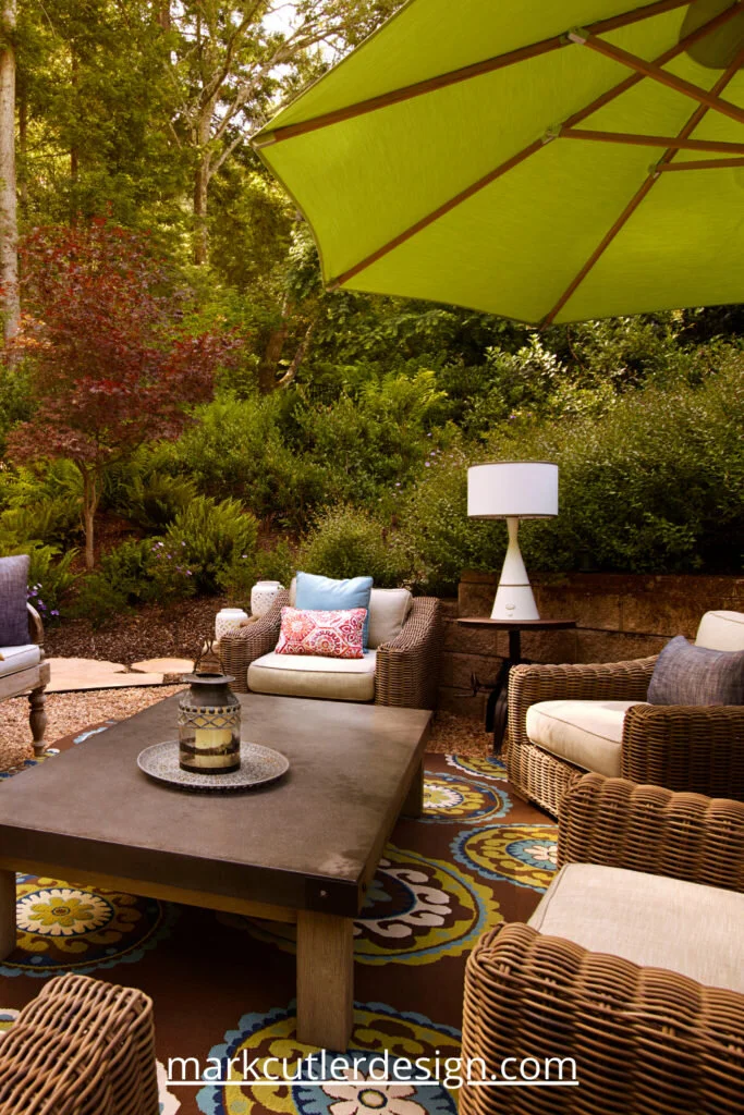 This outdoor space in a wooded setting in Northern California has wicker furniture placed around a wooden coffee table. An outdoor rug anchors the space.
