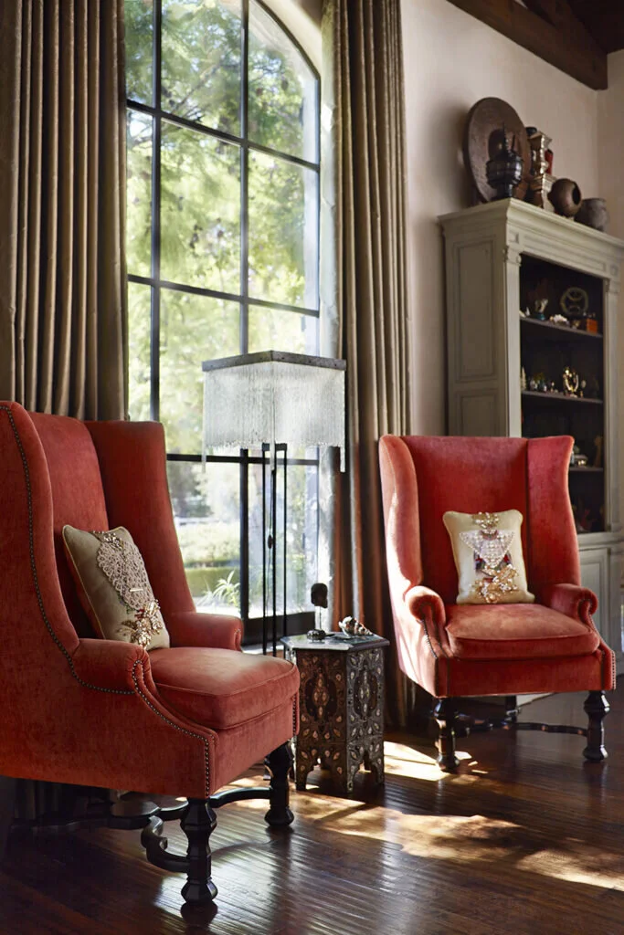 Burnt orange colored wingback chairs frame a large arched window. The chairs are adorned with beaded pillows.